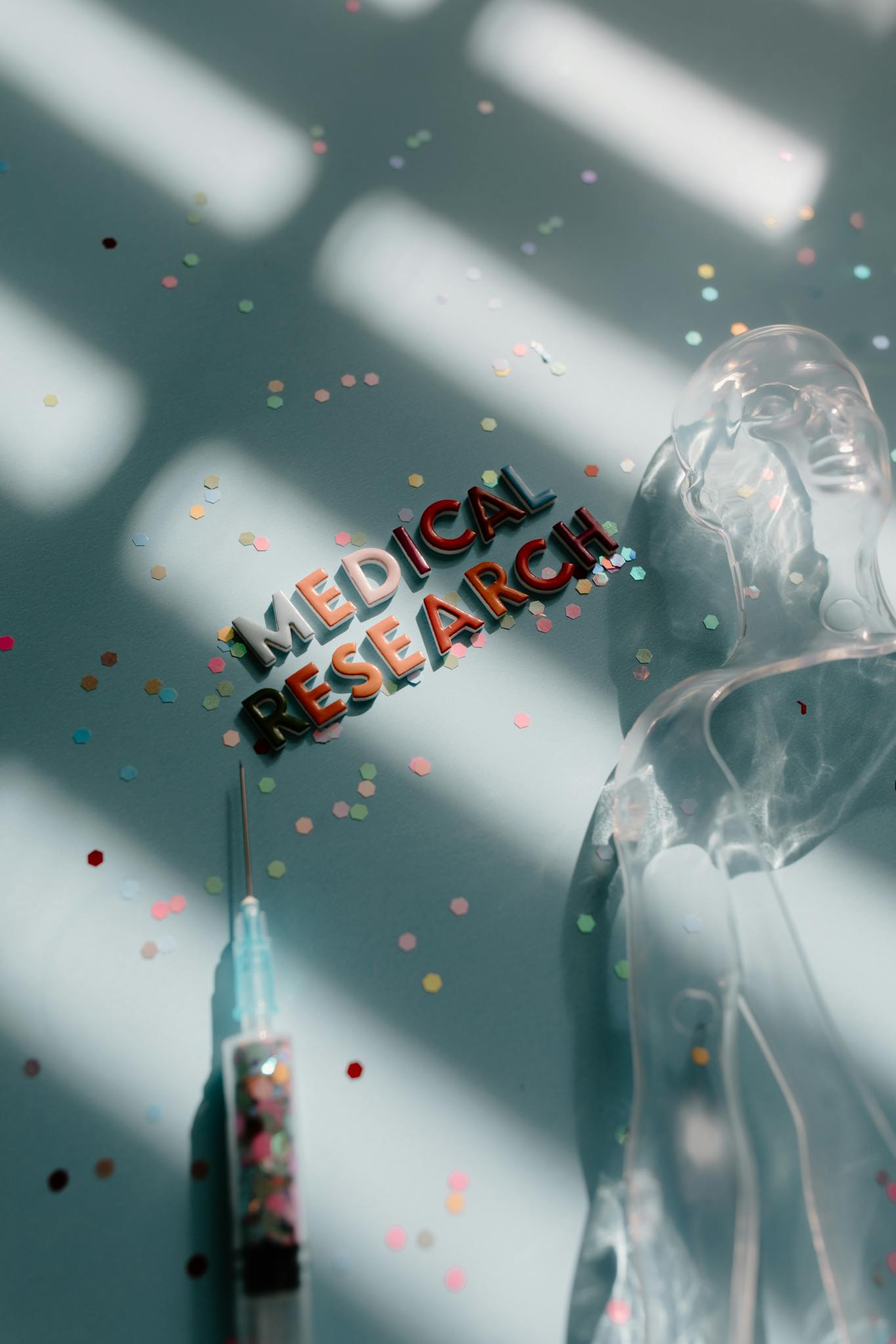 Creative depiction of medical research with syringe and confetti on a blue background.